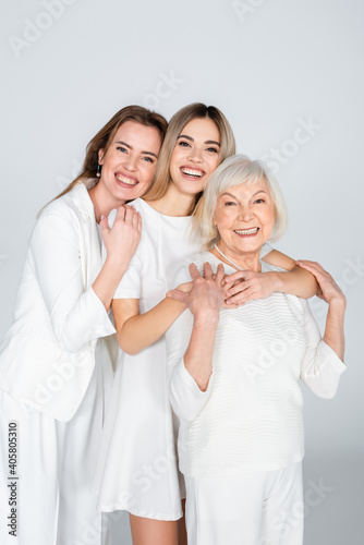 фотографія three generation of smiling women looking at camera and hugging isolated on grey