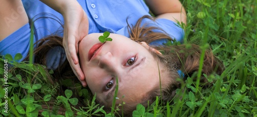 A young beautiful girl, a teenager with a leaf of clover in her mouth lying on the grass in the Park on a warm day. The banner of relaxation, vacations, no school, healthy lifestyle, St. patrick's day