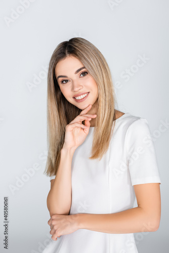 positive young woman in white outfit smiling isolated on grey