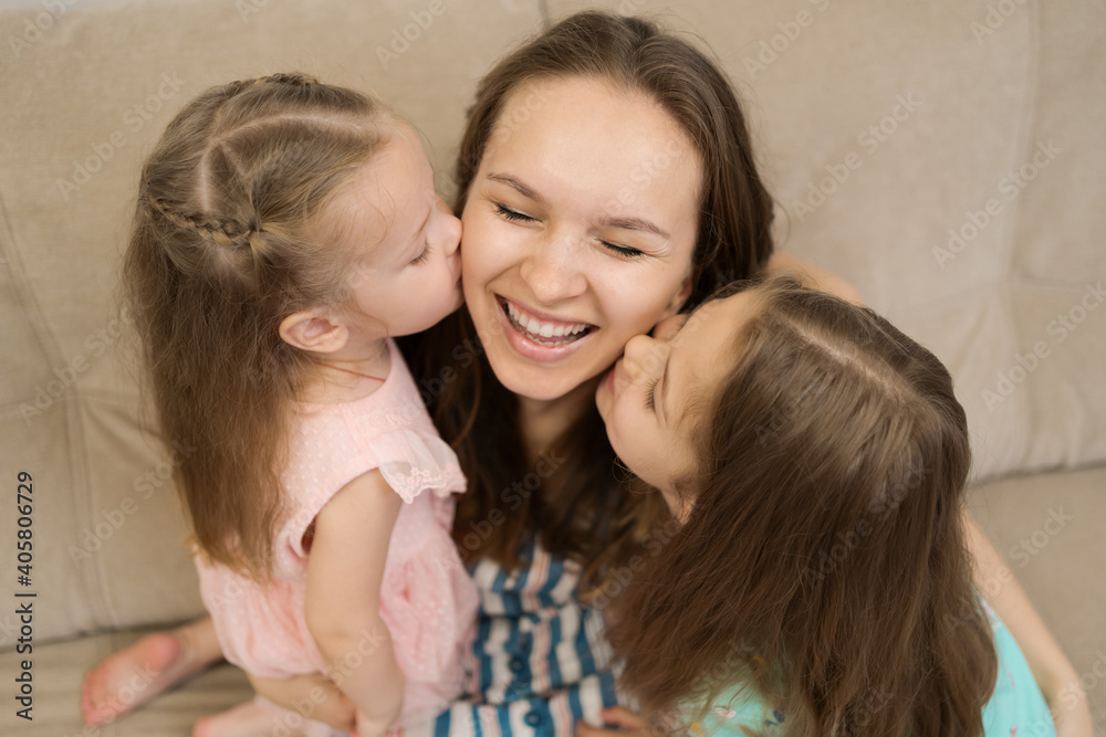 Lovely little daughters kissing sweet their sunny mother on checks. Happy family concept