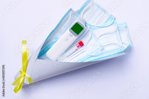 Non-contact thermometer, test for covid-19 and disposable medical masks in a ultimate gray bouquet with illuminating bowon a white background. Pandemic gift