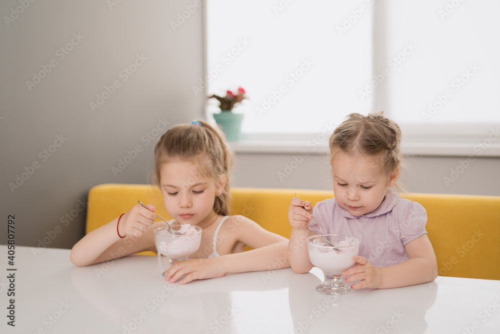 Little girl happily eat ice cream from a snail at a table in the kitchen