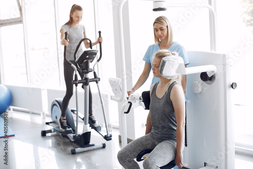 A woman is exercising in gym. She has a rehabilitation. A therapist is helping the woman to do the exercises.