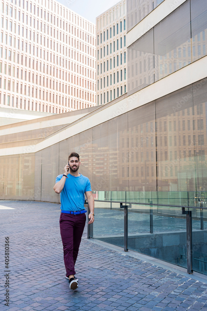 Portrait of cheerful modern businessman speaking by phone and smiling while walking outdoors