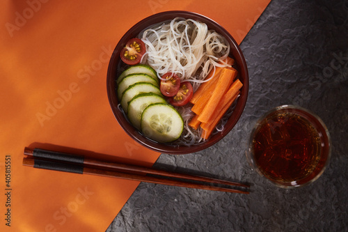 Asian noodle soup, Ramen with vegetables in a bowl. Gray-orange textured background top view. Ingredients carrots, cucumbers, tomatoes, noodles.