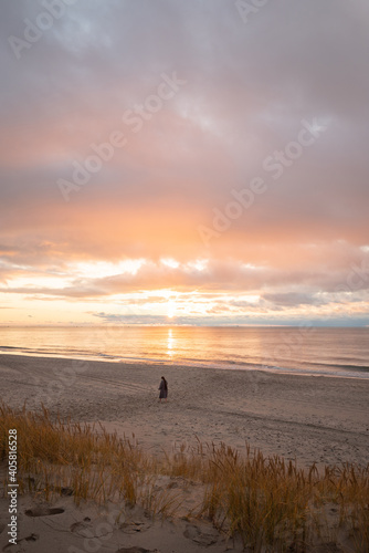 Wonderful golden sunset on the beach. A girl in the distance admires the sea and the sunset.