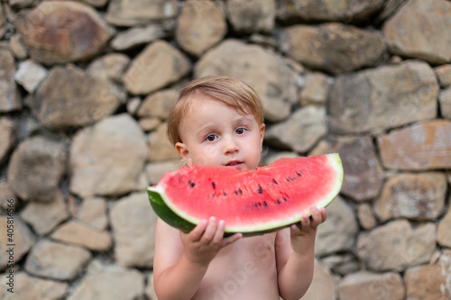 Child eating watermelon in the garden during summer vacances. Kids eat fruit outdoors. Healthy snack for children. Little bpy playing in the garden holding a slice of water melon. photo