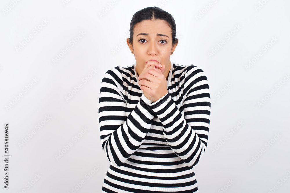 Young beautiful woman wearing stripped t-shirt against white background freezing, warming up hands, feels cold as she ran from office to buy cup of coffee. Young beautiful woman wearing stripped t-shirt against white background freezing, warming up hands, feels cold as she ran from office to buy cup of coffee.