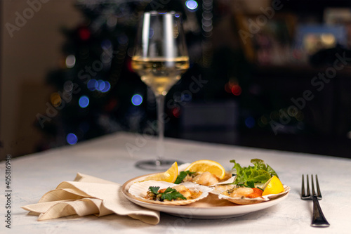 Baked scallops with caviar in a plate against the background of blurred glasses of wine. Scallops with lemon on a black background with a napkin and a fork.