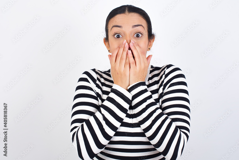 Vivacious Young beautiful woman wearing stripped t-shirt against white background, giggles joyfully, covers mouth, has natural laughter, hears positive story or funny anecdote Vivacious Young beautiful woman wearing stripped t-shirt against white background, giggles joyfully, covers mouth, has natural laughter, hears positive story or funny anecdote