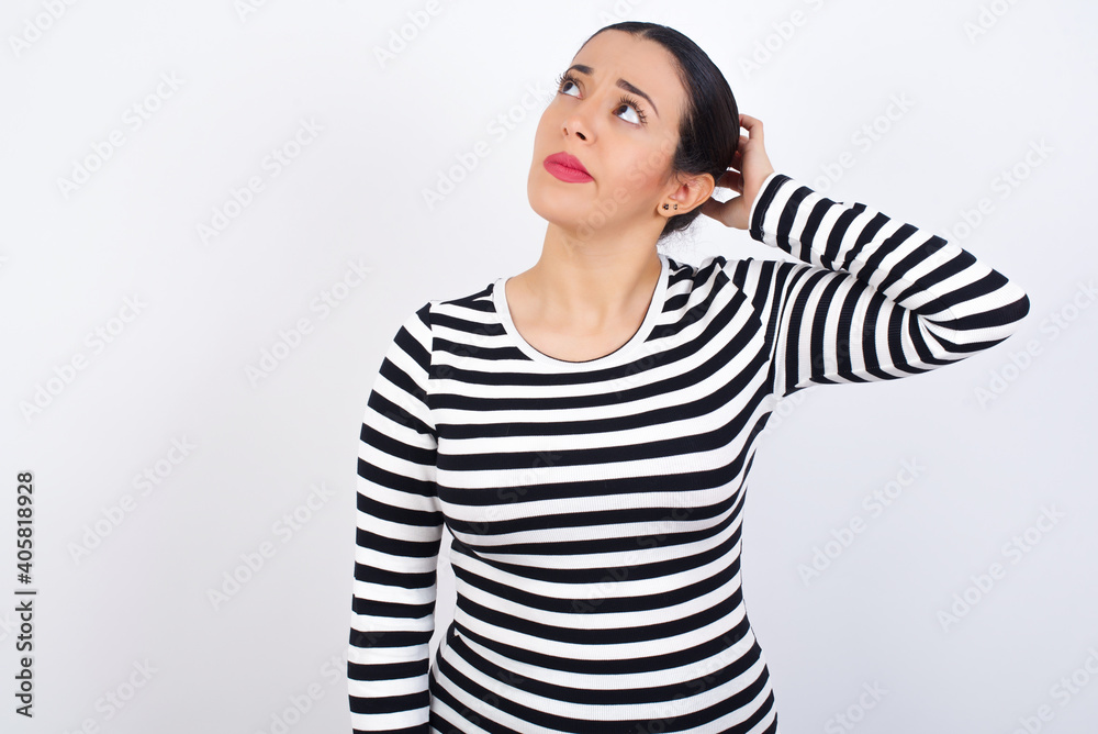 Young beautiful woman wearing stripped t-shirt against white background confuse and wonder about question. Uncertain with doubt, thinking with hand on head. Pensive concept. Young beautiful woman wearing stripped t-shirt against white background confuse and wonder about question. Uncertain with doubt, thinking with hand on head. Pensive concept.