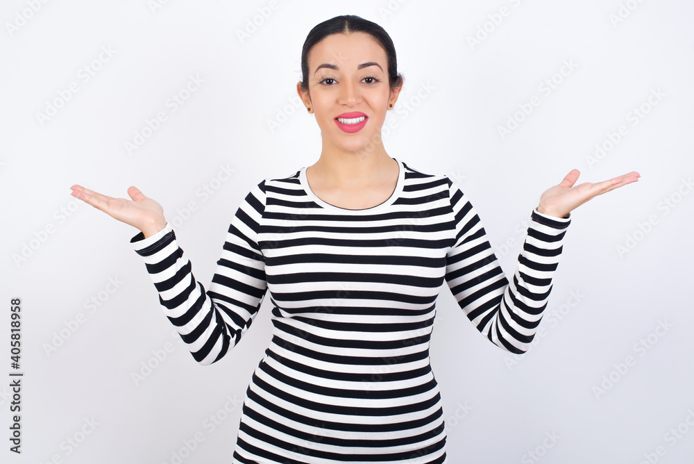 Cheerful cheery optimistic Young beautiful woman wearing stripped t-shirt against white background holding two palms copy space Cheerful cheery optimistic Young beautiful woman wearing stripped t-shirt against white background holding two palms copy space