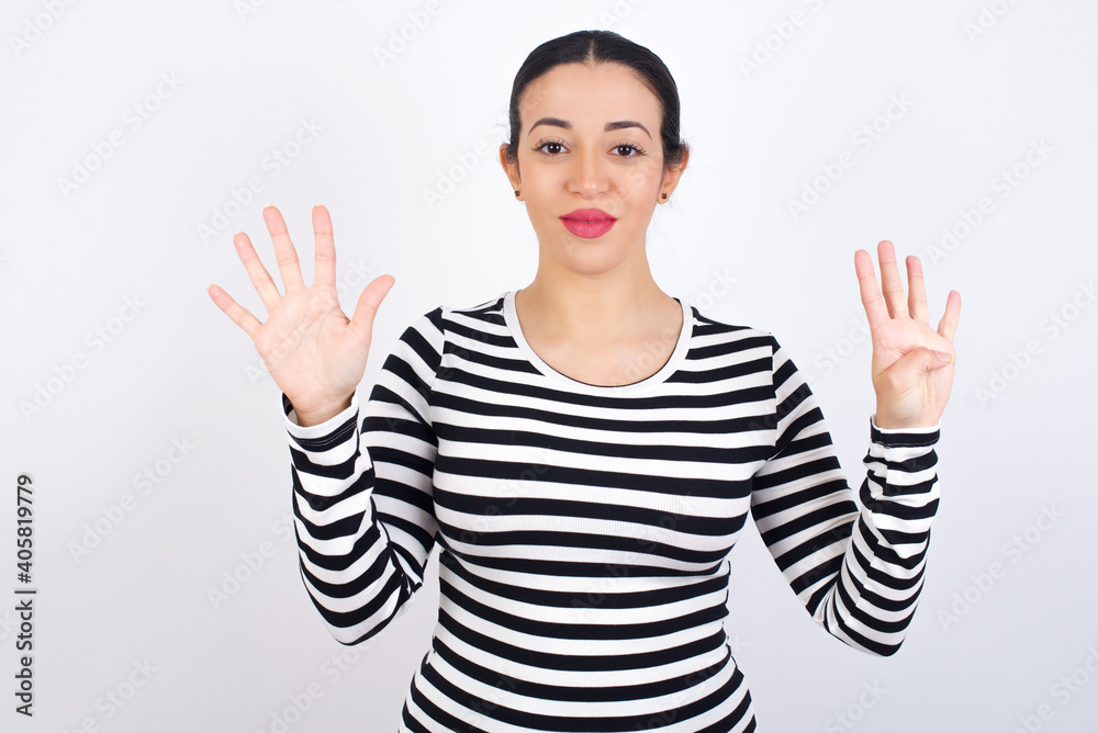 Young beautiful woman wearing stripped t-shirt against white background showing and pointing up with fingers number nine while smiling confident and happy. Young beautiful woman wearing stripped t-shirt against white background showing and pointing up with fingers number nine while smiling confident and happy.