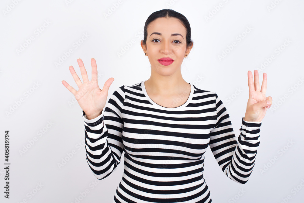 Young beautiful woman wearing stripped t-shirt against white background showing and pointing up with fingers number eight while smiling confident and happy. Young beautiful woman wearing stripped t-shirt against white background showing and pointing up with fingers number eight while smiling confident and happy.