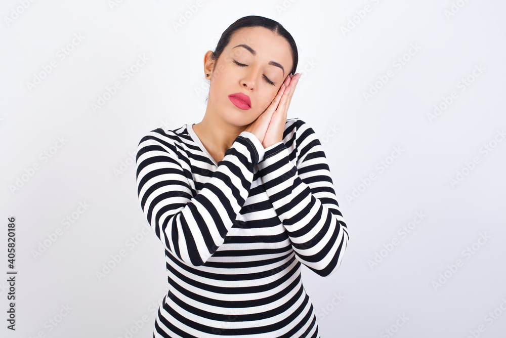 Young beautiful woman wearing stripped t-shirt against white background sleeping tired dreaming and posing with hands together while smiling with closed eyes. Young beautiful woman wearing stripped t-shirt against white background sleeping tired dreaming and posing with hands together while smiling with closed eyes.