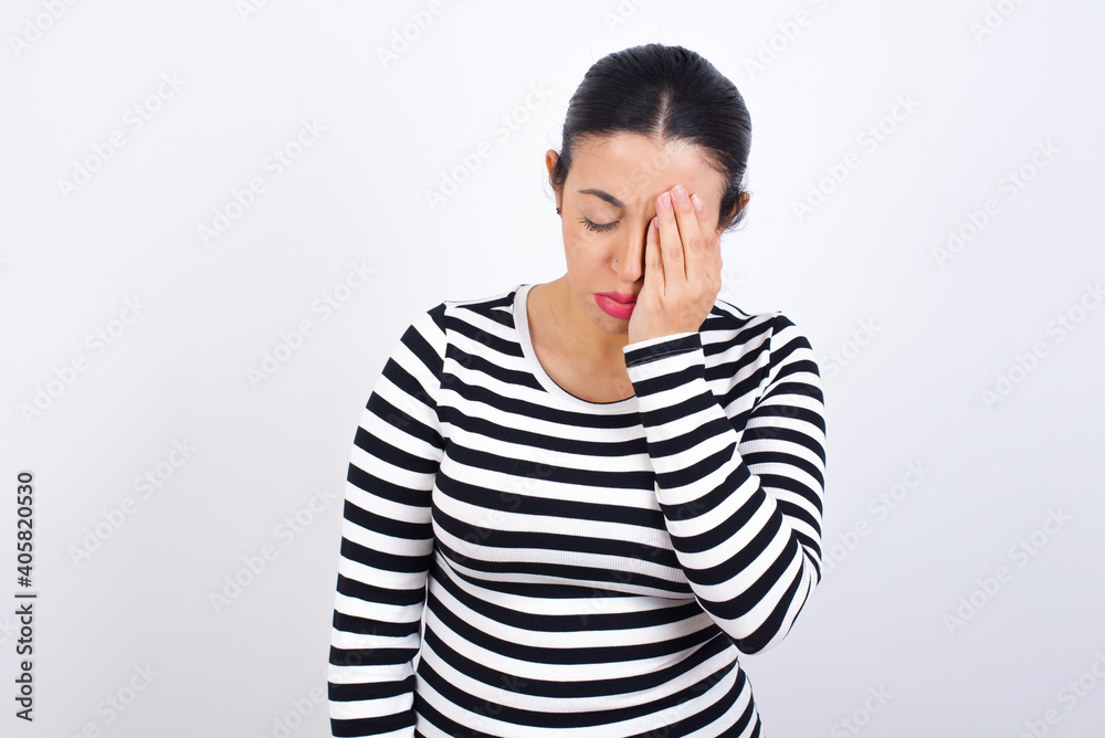 Tired overworked Young beautiful woman wearing stripped t-shirt against white has sleepy expression, gloomy look, covers face with hand, has eyes shut, gasps from tiredness, fatigue after party Tired overworked Young beautiful woman wearing stripped t-shirt against white has sleepy expression, gloomy look, covers face with hand, has eyes shut, gasps from tiredness, fatigue after party