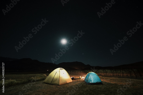 Camping in the mountains under the moon. A tent pitched up and glowing under the sky.