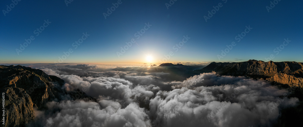 Beautiful scenic mountain landscape with morning mountains, cloudy blue sky and light of rising sun at the hazy horizon.