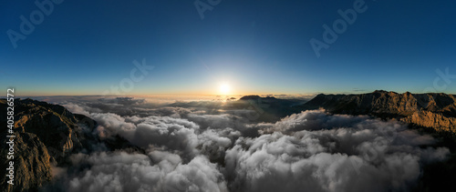 Beautiful scenic mountain landscape with morning mountains, cloudy blue sky and light of rising sun at the hazy horizon.