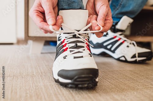 Man tying laces on black and white leather winter sneakers before going outside