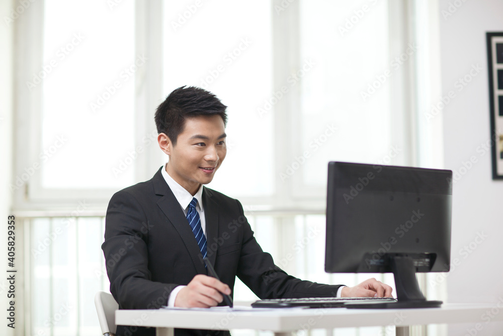 Portrait of businessman sitting at desk,looking at computer Portrait of businessman sitting at desk,looking at computer