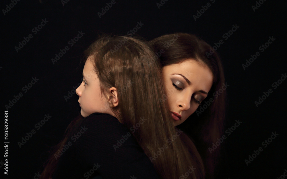 Sad serious thinking daughter hugging her unhappy mother with pensive face on black background in dark shadow. Closeup family Sad serious thinking daughter hugging her unhappy mother with pensive face on black background in dark shadow. Closeup family