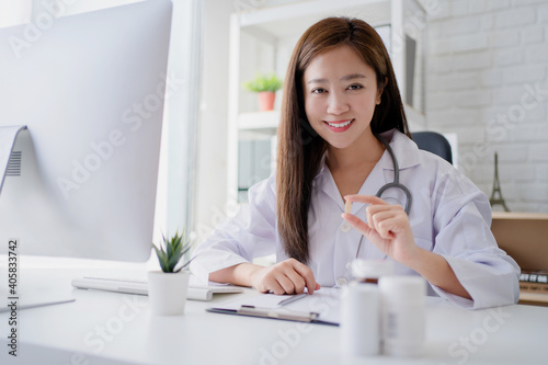 Young woman doctor or pharmacist sitting at a desk holding a medicine in her hand. Concept of medical care pharmacy.