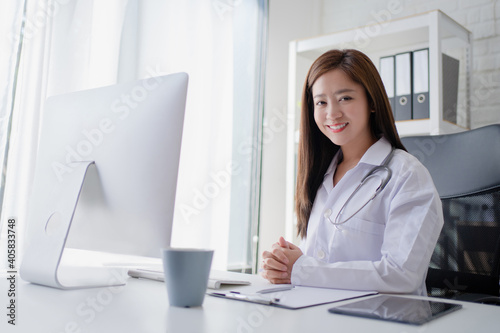Female doctor working at office desk and smiling at camera with office interiors on the background.