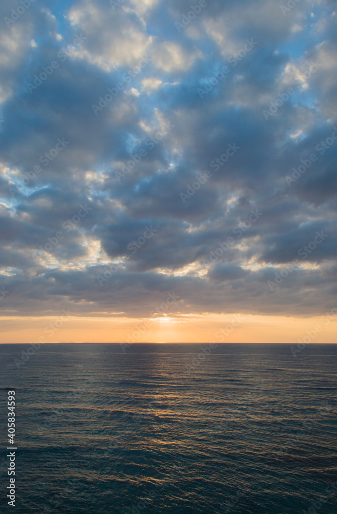 夕暮れの雲の多い空とオレンジ色の太陽光が反射する海