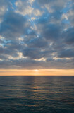夕暮れの雲の多い空とオレンジ色の太陽光が反射する海