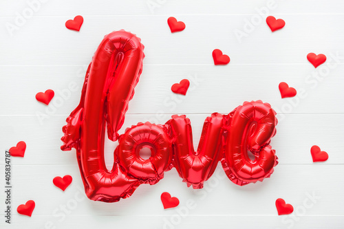 Red foil balloon in shape of word Love and textile hearts on white wooden background. Valentine's Day, love concept. Flat lay, top view.