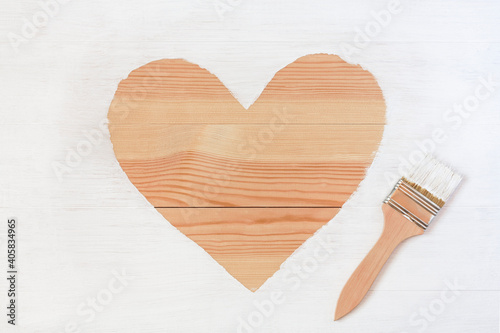Heart shape pattern and paintbrush on wooden surface painted with white paint. Home renovation, construction concept. Top view, copy space.