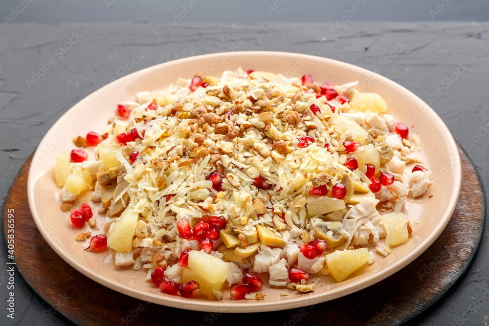 A plate with salad with chicken, pineapple, pomegranate and nuts on a concrete background on a wooden stand close-up.