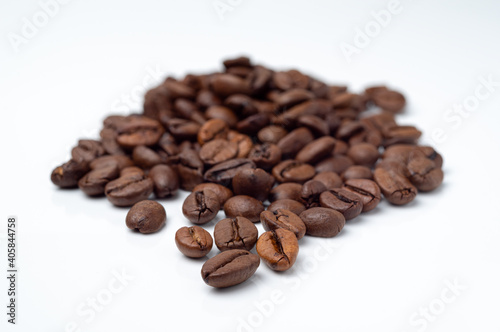 Dark  roasted coffee beans pile on a white surface. 