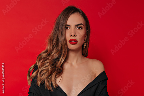 Studio portrait of elegant stylish lady with evening make-up in black dress with bare shoulders over red background in Valentine's day