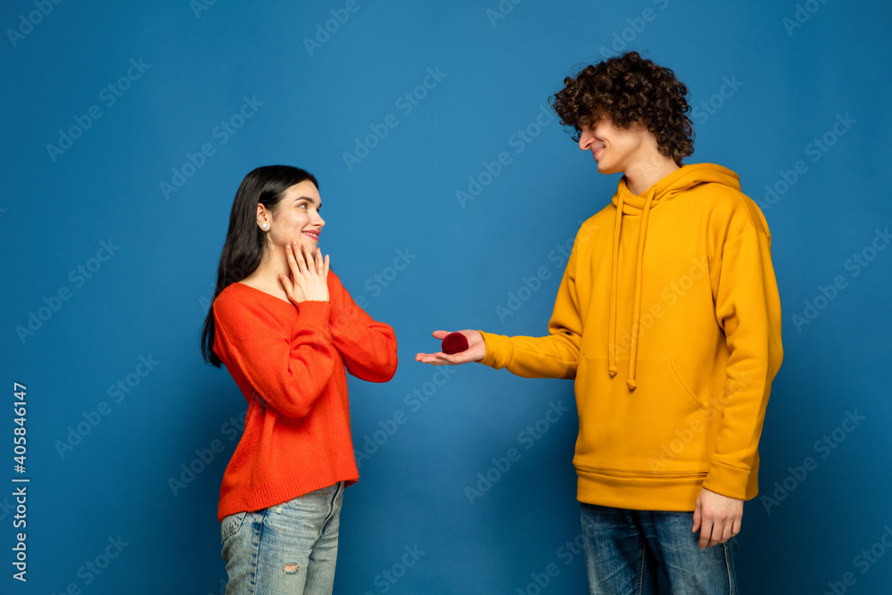 Marriage proposal. Beautiful couple in love on blue studio background. Saint Valentine's Day, love, relationship and human emotions concept. Copyspace. Young man and woman look happy together. Marriage proposal. Beautiful couple in love on blue studio background. Saint Valentine's Day, love, relationship and human emotions concept. Copyspace. Young man and woman look happy together.