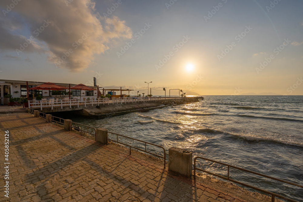 Sunset over the Mediterannean sea. Beautiful landscape of sandy beach with sea waves and wooden pier during sunset. Sky reflections in water.