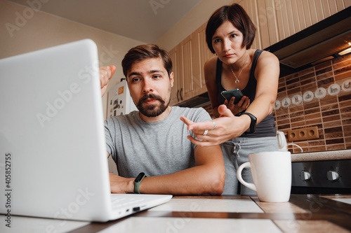 Couple at kitchen, reading news and using laptop.