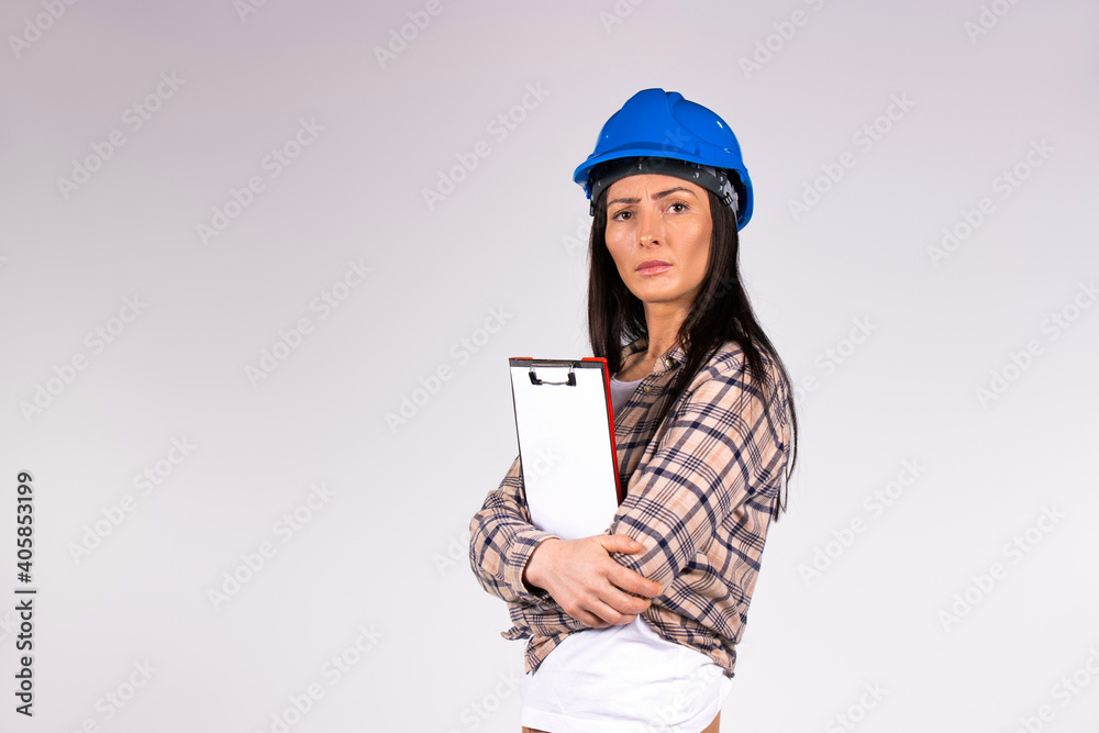Serious female engineer with a folder in hands looking at the camera on a gray background with blank space. Serious female engineer with a folder in hands looking at the camera on a gray background with blank space.