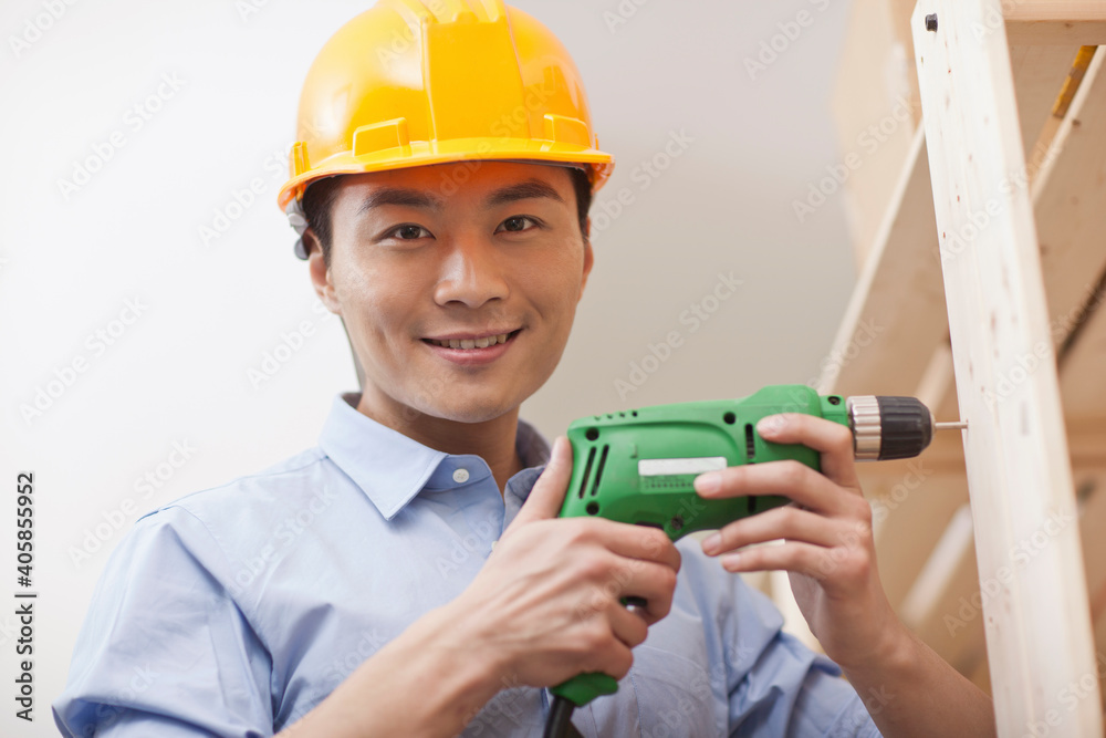Portrait of young workman using electric drill in office,close-up Portrait of young workman using electric drill in office,close-up