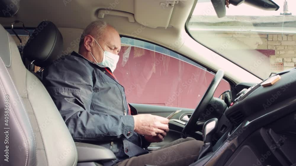 A business man in a car takes and counts money. Confident mature businessman working remotely. Professional activity for the purchase and sale of goods. Happy male of Caucasian appearance in autumn. A business man in a car takes and counts money. Confident mature businessman working remotely. Professional activity for the purchase and sale of goods. Happy male of Caucasian appearance in autumn.