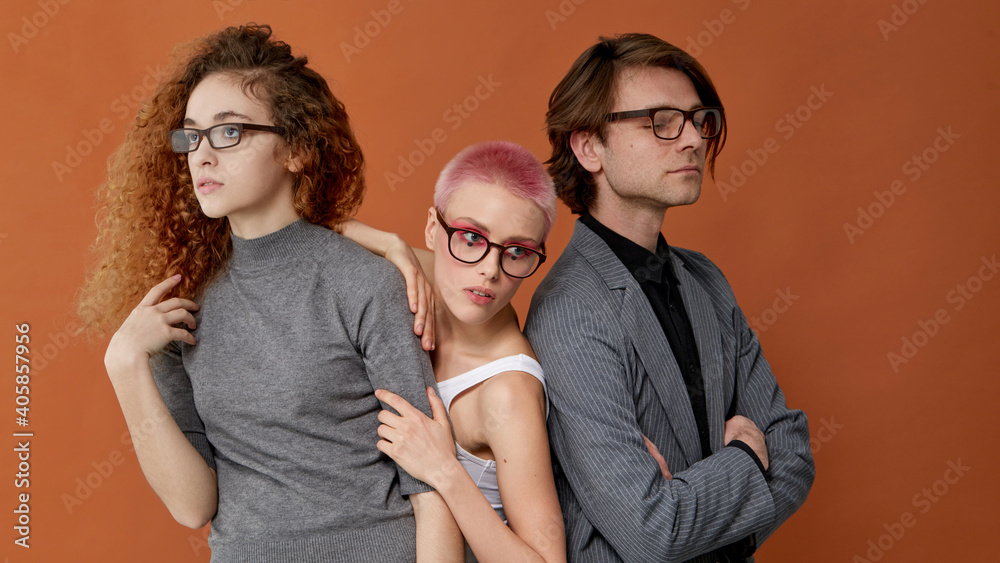 Front portrait of three youngs caucasian stylish models in casual clothes, wear eyeglasses, over brown background. Front portrait of three youngs caucasian stylish models in casual clothes, wear eyeglasses, over brown background.