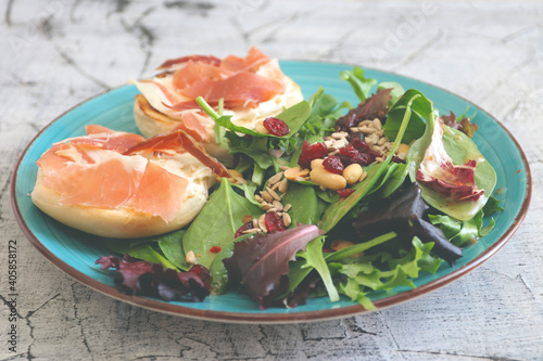 Breakfast of fresh salad and two halves of a bagel with cheese and prosciutto.