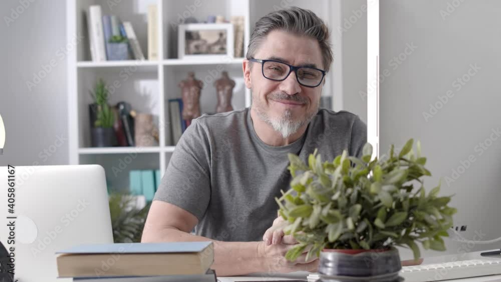 Portrait of happy older man in glasses sitting at desk working with laptop in home office. Confident 50s businessman in casual with gray hair smiling. Portrait of happy older man in glasses sitting at desk working with laptop in home office. Confident 50s businessman in casual with gray hair smiling.