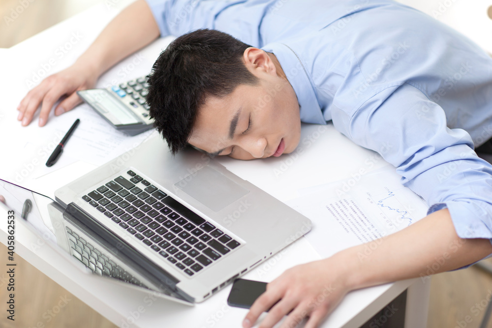 © eastfenceimage - Portrait of young businessman sleeping on laptop by desk