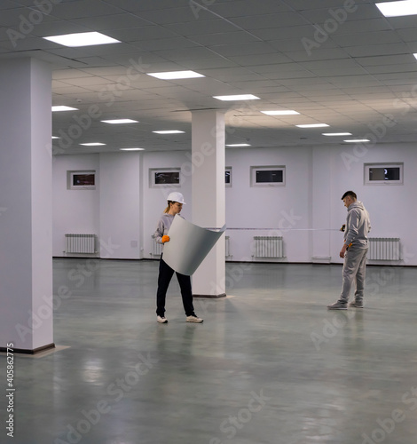 Workers measure the distance with a tape measure. A man and a woman in work clothes measure the room with a tape measure, referring to the drawings.