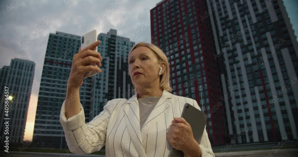 Professional female broker having videocall on cellphone near new skyscrapers Professional female broker having videocall on cellphone near new skyscrapers