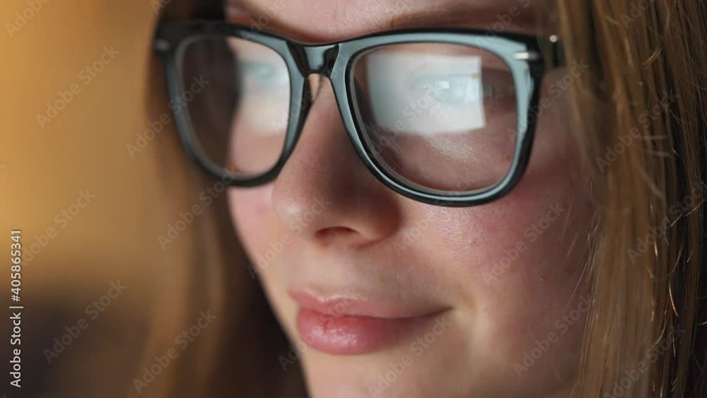 Woman in glasses looking on the monitor and surfing Internet. The monitor screen is reflected in the glasses. Work at night. Home Office. Remote work Woman in glasses looking on the monitor and surfing Internet. The monitor screen is reflected in the glasses. Work at night. Home Office. Remote work