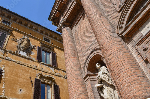 Detail of the façade of the Church of St Christopher with the statue of St Bernardo Tolomei and an ancient palace with a stone coat of arms in the background, Siena, Tuscany, Italy photo