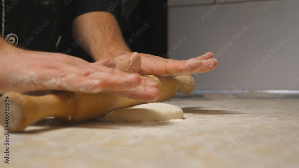Close up arms of cook unrolling pastry using rolling pin on a kitchen table at restaurant. Male hands of chef rolling out dough on a wooden surface at cuisine. Process of making pizza. Slow motion Close up arms of cook unrolling pastry using rolling pin on a kitchen table at restaurant. Male hands of chef rolling out dough on a wooden surface at cuisine. Process of making pizza. Slow motion